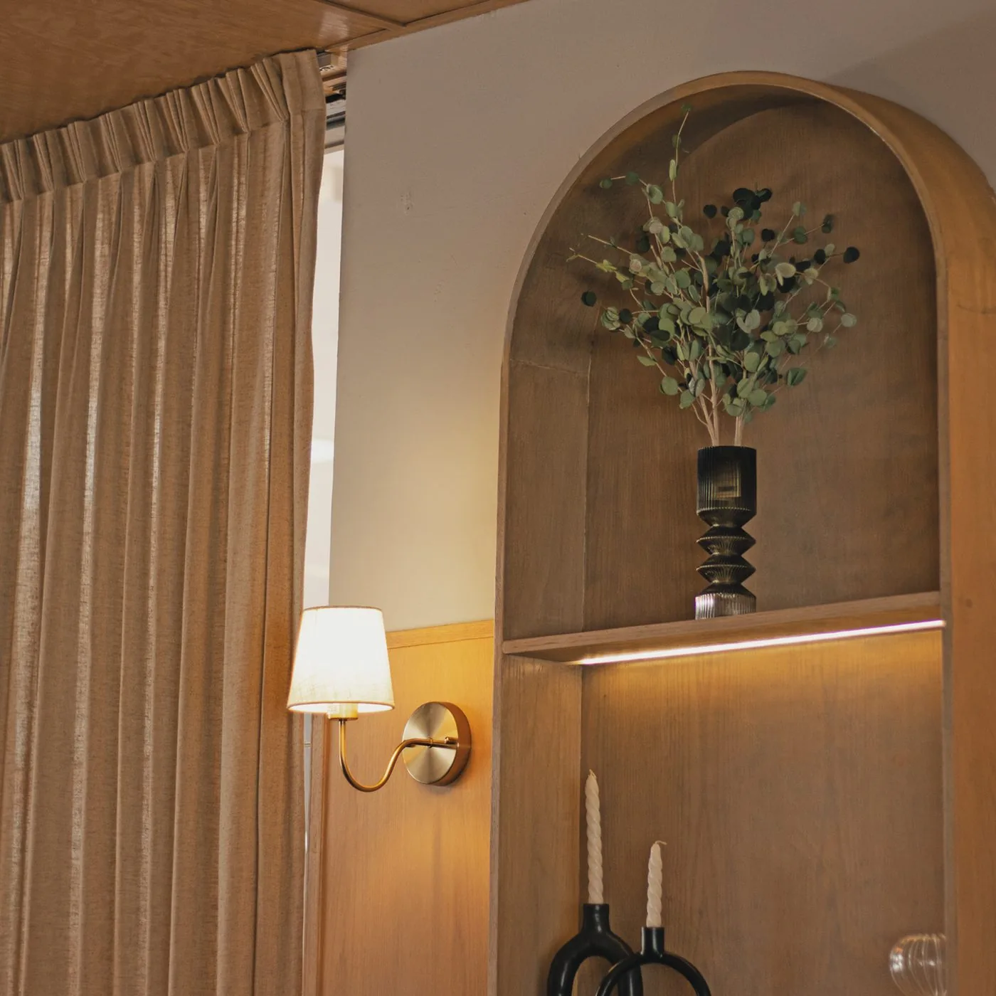 Nicho de madera en arco con una lámpara de pared y cortinas de lino
