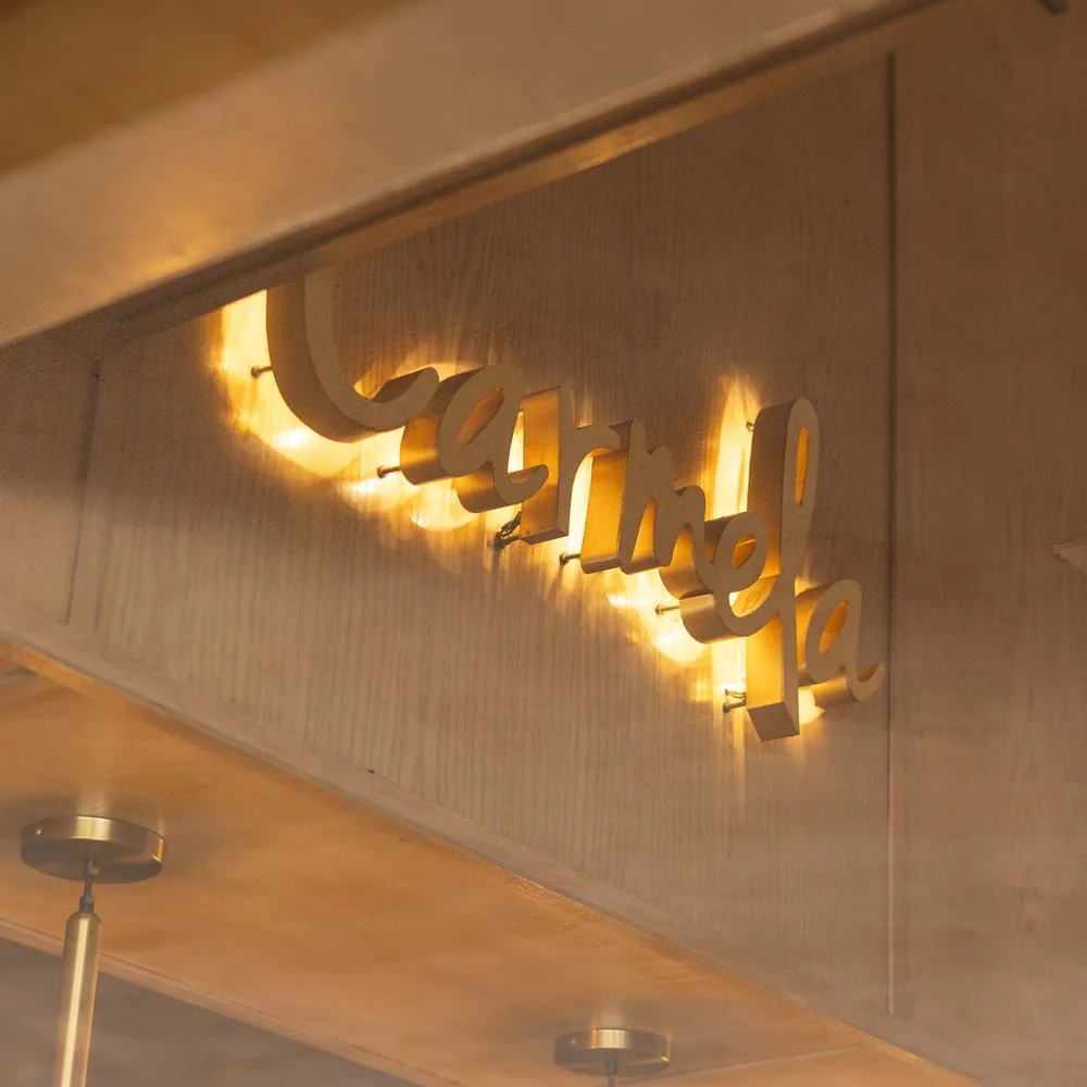 El letrero de Carmela iluminado sobre el muro de madera