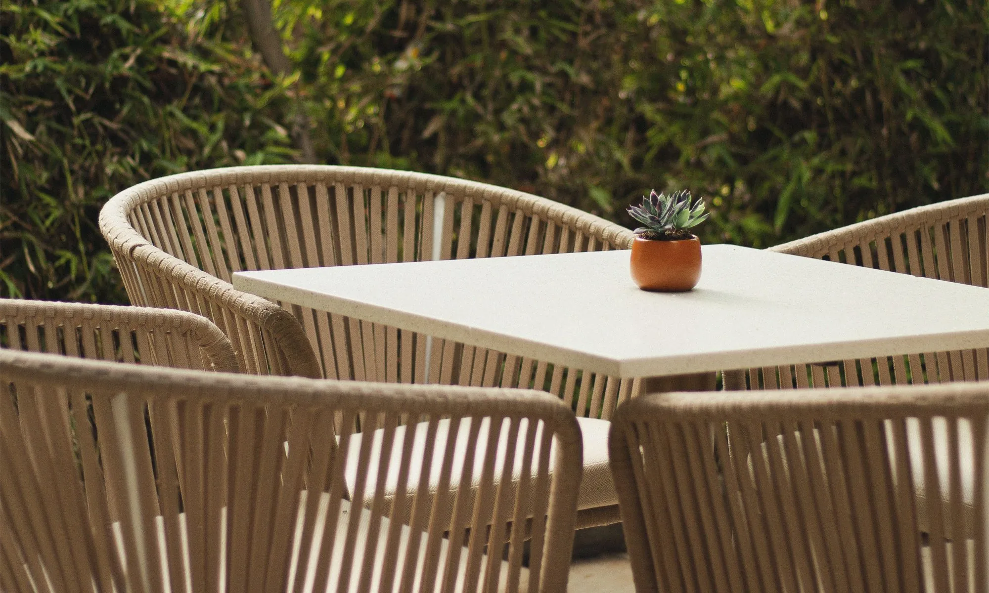 Terraza de Carmela Primavera: mesa blanca y sillas tejidas frente al jardín