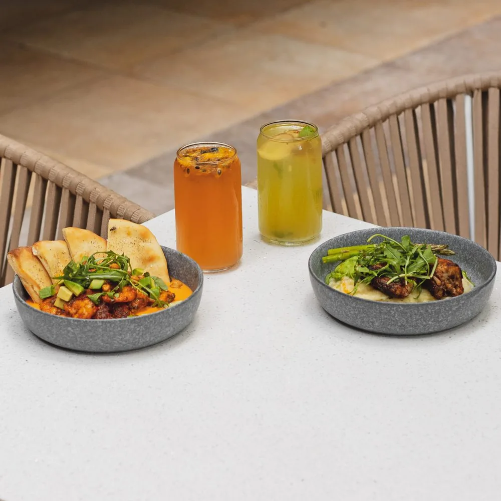 Dos platillos y dos bebidas sobre una mesa blanca de la terraza