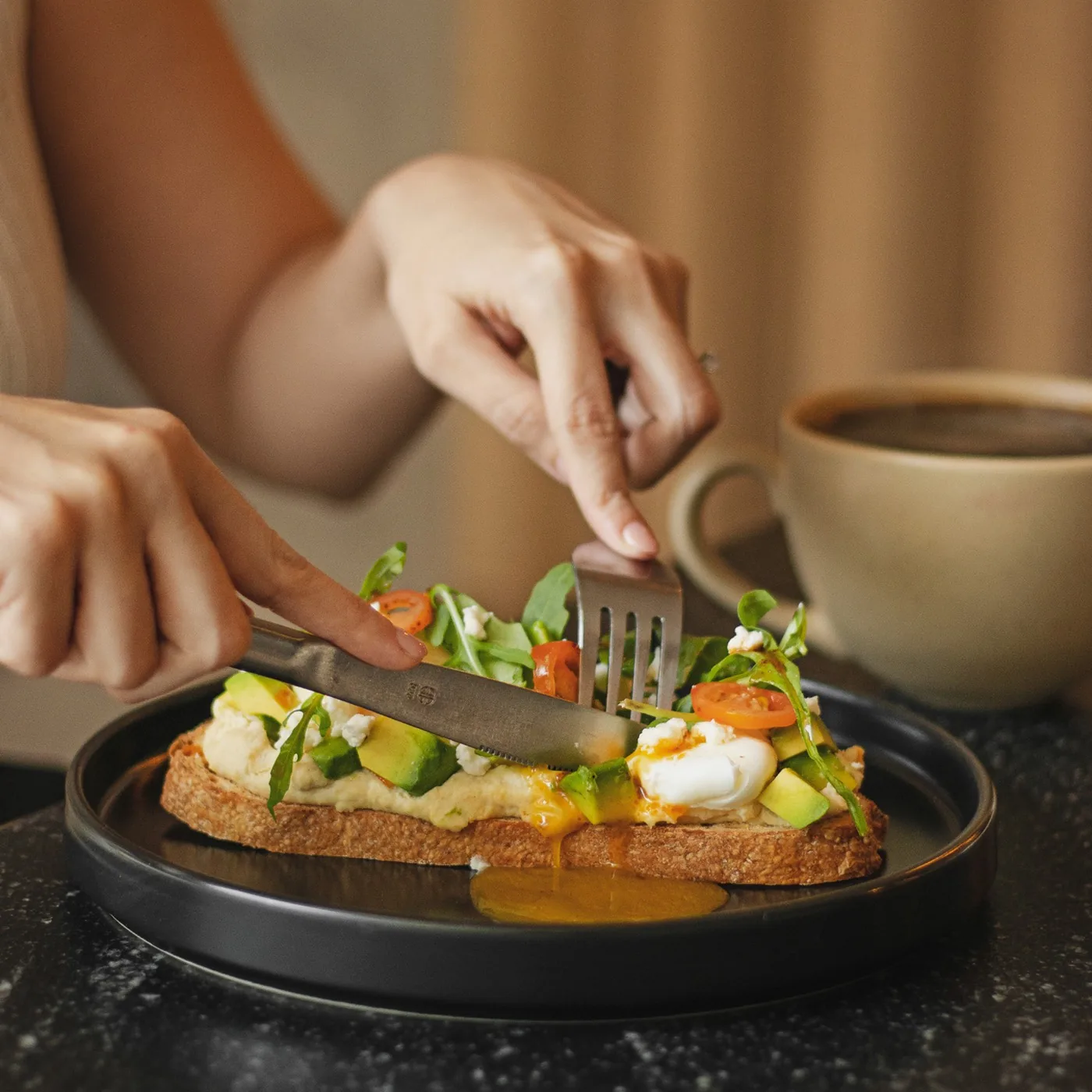 Manos partiendo una tosta junto a una taza de café